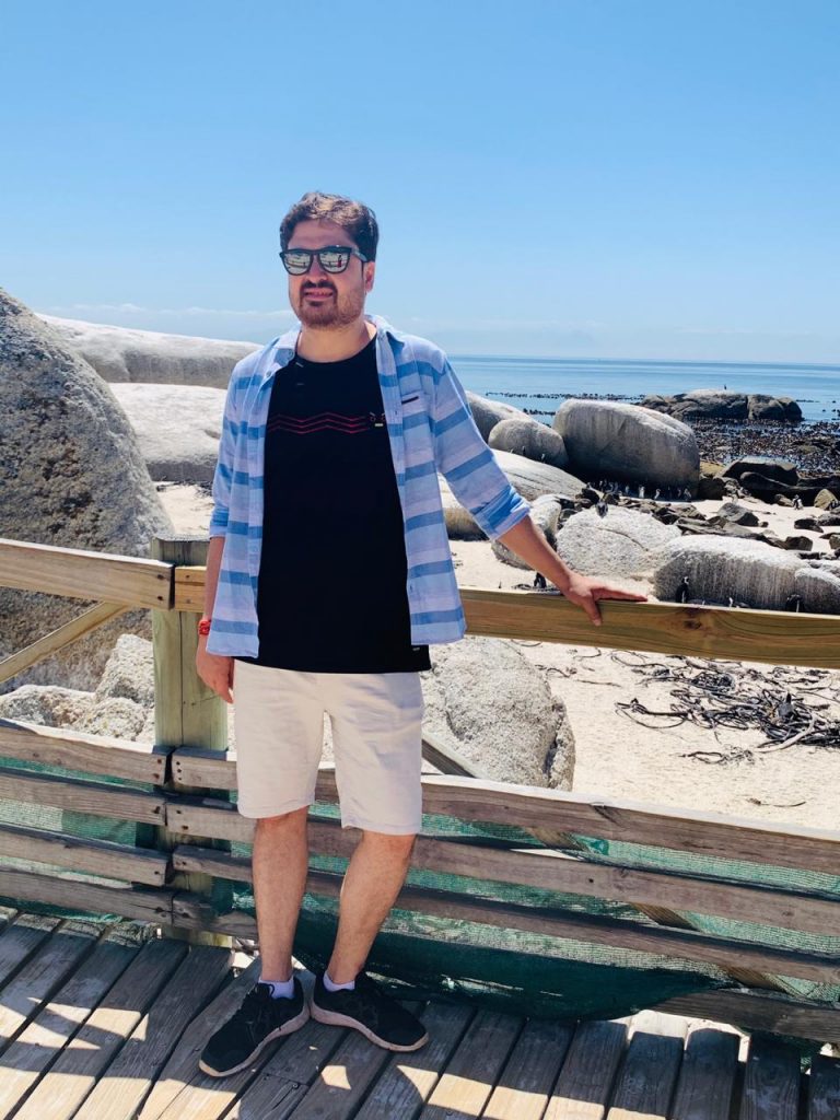 A picture of a man posing with the beach as the backdrop