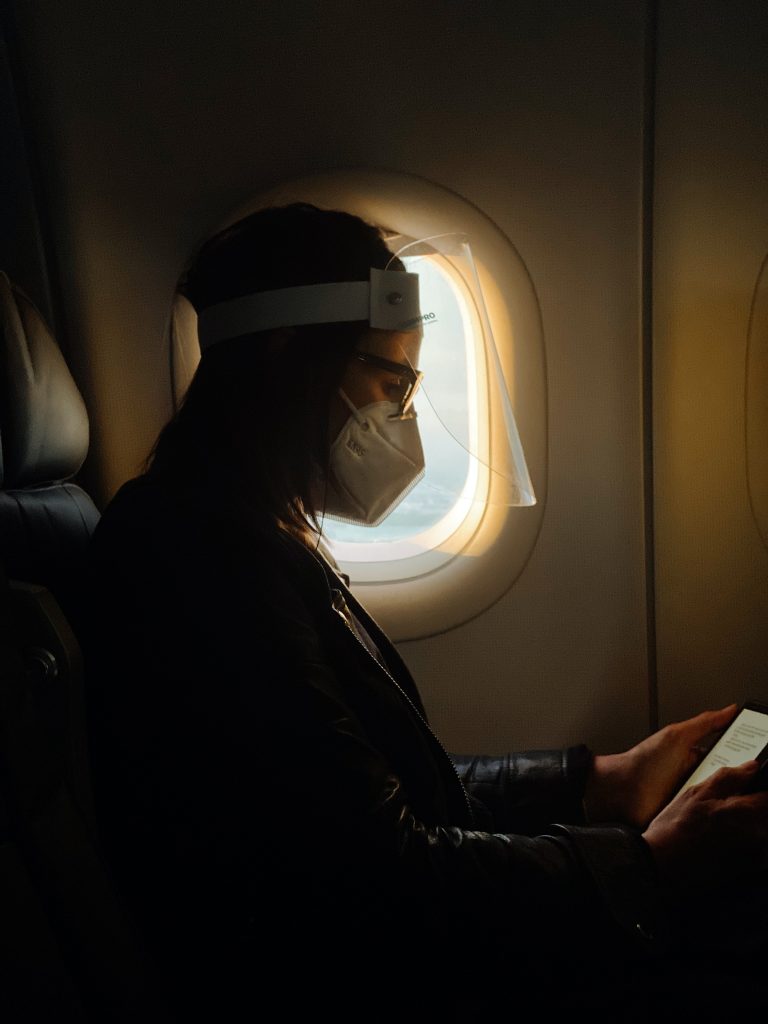 A lady sitting inside the flight, wearing a mask